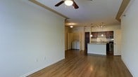 This single-floor residence features an open-concept living and kitchen layout unified by warm hardwood-style flooring throughout. The living area is spacious and bright, highlighted by a ceiling fan with a light fixture and clean, neutral-toned walls that create a versatile backdrop for any décor style.

The kitchen is positioned along one side of the open floor plan and includes dark cabinetry, a granite or stone-look countertop, and a breakfast bar overhang that provides casual seating. A combination of pendant lights and a track lighting system illuminates the kitchen workspace effectively. A sink is integrated into the kitchen island, adding functional convenience to the layout.

Adjacent to the kitchen and living area is a dedicated laundry nook, which accommodates a side-by-side washer and dryer. This in-unit laundry space adds a practical, self-contained amenity without disrupting the flow of the main living area.

The overall ambiance is clean, modern, and functional, with a cohesive design that connects the living, cooking, and utility spaces seamlessly on a single level.