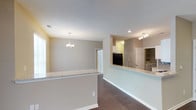 This single-floor, 3-bedroom, 2-bathroom residence offers a thoughtfully designed open-concept layout that promotes a seamless flow between the living, dining, and kitchen areas. The interior is finished with rich hardwood-style flooring throughout the main living spaces, providing a warm and cohesive aesthetic.

The kitchen is a standout feature, showcasing granite countertops with a breakfast bar that opens directly to the dining and living areas — ideal for entertaining or everyday living. Dark appliances, including a refrigerator, complement the cabinetry, and a modern faucet adds a functional yet stylish touch. Track lighting above the kitchen ensures the workspace is well-illuminated.

The dining area is accentuated by an elegant chandelier, adding a classic decorative element to the space. Neutral, warm-toned walls throughout create a versatile backdrop that complements a variety of interior styles. A textured ceiling adds subtle visual interest across all rooms.

Natural light filters in through windows in the living area, brightening the space without overwhelming it. Additional rooms, including what appears to be a walk-in closet or utility space, are accessible through interior doors, contributing to the home's practical and well-organized floor plan.