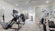 Located at 445 Warfield Blvd in Clarksville, Tennessee, this fitness center offers a generously sized, single-floor layout designed to accommodate a comprehensive workout experience. The space is finished with refined architectural details, including crown molding, chair rail wainscoting, and soft sage-green walls that create a clean, welcoming ambiance throughout.

The flooring consists of durable patterned carpet tiles, providing comfort underfoot during workouts. Recessed lighting and multiple large ceiling fans ensure the space remains well-lit and well-ventilated. Natural light flows in through windows at the far end of the room, where glass doors provide an exit to the outdoors.

The fitness floor is thoughtfully arranged to maximize usability. One end of the room houses cardio equipment, including multiple treadmills and a stair climber. Moving through the space, users will find an array of strength training stations, including a multi-function cable machine, leg press, weight benches with barbell racks, and a cable crossover system. Additional accessories such as resistance bands, medicine balls, and yoga mats are neatly organized near the entrance. Wall-mounted flat-screen televisions and mirrors are positioned throughout to enhance the workout experience. The layout allows for comfortable movement between stations, making this fitness center a functional and attractive amenity.