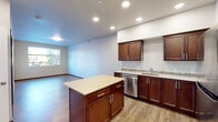 This well-appointed single-floor residence offers a thoughtfully designed open-concept layout that seamlessly connects the kitchen and living areas. The kitchen serves as the centerpiece of the home, featuring rich dark-wood cabinetry, light quartz countertops, a central island with additional storage, and a full suite of stainless steel appliances including a refrigerator, range, built-in microwave, and dishwasher. A mosaic tile backsplash adds a refined decorative touch, while recessed lighting illuminates the space throughout. Hardwood-style flooring extends across the main living and kitchen areas, lending warmth and continuity to the open floor plan. A generously sized living area is bathed in natural light from large windows that frame views of surrounding greenery, with a glass-paneled exterior door providing direct outdoor access. The bedroom is comfortably carpeted and benefits from a window overlooking a wooded outdoor setting. The bathroom is finished with a wide quartz vanity, dark wood cabinetry, a mosaic tile backsplash, and a large mirror. An in-unit laundry area is conveniently tucked nearby. The overall aesthetic is clean, modern, and move-in ready, with consistent finishes throughout.