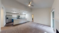 This single-floor residence is defined by its striking vaulted ceilings, which lend an expansive, airy quality to the open-concept living and kitchen area. The living room is finished with plush neutral carpet, a ceiling fan, and a tiled fireplace with a clean white mantel, creating a comfortable focal point. A sliding glass door allows additional natural light to filter into the space.

The kitchen is a standout feature, showcasing bold teal lower cabinetry paired with crisp white upper cabinets and a textured tile backsplash. Granite-look countertops extend across the surfaces and onto a generous center island complete with an undermount sink and pendant lighting overhead. Stainless steel appliances, including a range, microwave, and refrigerator, complete the well-equipped cooking space. Dark hardwood-style flooring runs throughout the kitchen, providing a sharp contrast to the carpeted living areas.

The bedroom is a well-proportioned room with carpet, a ceiling fan, and a window with outdoor views. Two full bathrooms are present, each featuring a tub-shower combination with white tile surround, dark wood-style flooring, chrome fixtures, and granite-topped vanities, maintaining a consistent, clean aesthetic throughout the unit.