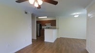 This single-floor space offers a thoughtfully designed open-concept layout that connects the living area and kitchen in a seamless flow. The living area features warm hardwood-style flooring that extends throughout, complemented by crown molding along the upper walls and a ceiling fan that adds both function and character to the space. Natural light fills the room, highlighting the clean, neutral wall tones that create a bright and welcoming ambiance. The kitchen is a standout feature, showcasing rich, dark wood cabinetry that provides ample storage, paired with a white peninsula that serves as both a workspace and a casual dining counter. Stainless steel appliances, including a refrigerator and a white range with an overhead ventilation hood, complete the kitchen setup. Recessed under-cabinet lighting adds a practical touch to the cooking area. The textured ceiling adds a subtle architectural detail throughout the space. Crown molding trims the transition between walls and ceiling, lending a classic, finished look. Overall, the space combines functional design with warm, inviting finishes, making it well-suited for comfortable everyday living.