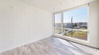 Located at 1942 Fawcett Ave in Tacoma, WA, this 2-bedroom, 1-bathroom unit offers a efficiently designed layout across a single floor. Light wood-style flooring runs throughout, providing a clean, cohesive aesthetic that brightens the interior. The unit is organized along a central corridor lined with recessed ceiling lights, leading from the entry toward the living and kitchen area. The kitchen features dark wood-toned cabinetry paired with stainless steel appliances, including a full-size refrigerator, and is compactly integrated into the layout to maximize usable space. The primary bedroom is a notable highlight, boasting a large floor-to-ceiling window that frames outdoor views of the Tacoma cityscape and fills the room with abundant natural light. The second bedroom also benefits from natural light and includes a sliding door closet for storage. A dedicated closet space with built-in shelving provides additional organization. The bathroom is finished with a dark wood vanity, white countertop with an undermount sink, a large mirror, wood-style flooring, and a shower/tub combination. Clean white walls throughout lend the space a modern, neutral palette well-suited for personalization.