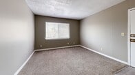 Located at 2100 N 57th St in Kansas City, KS, this one-bedroom, one-bathroom unit offers a well-organized single-floor layout designed for comfortable everyday living. Neutral taupe walls and textured ceilings carry throughout the space, creating a cohesive and understated aesthetic.

The kitchen is outfitted with warm honey-toned wood cabinetry, laminate countertops, and white appliances including an electric range, refrigerator, and a double-basin sink. Wood-look vinyl flooring adds durability and visual appeal to this functional cooking space.

The living room flows from the kitchen area and features soft carpet flooring, continuing into the hallway and bedroom. A window allows natural light to filter in, offering a view of the surrounding tree line. The bedroom is a comfortable size, featuring two side-by-side closets with panel doors that provide generous storage. An additional window in the bedroom brings in further natural light.

The bathroom includes a full-size soaking tub with an overhead shower, a clean white surround, and wood-look flooring that complements the rest of the unit. A hallway connects all rooms efficiently, completing this compact yet practical floor plan suited for single occupancy or couples.