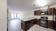 Located at 211 W Mulberry St in Baltimore's historic Mount Vernon neighborhood, this one-bedroom, one-bathroom unit offers a well-designed single-floor layout with a clean, modern aesthetic throughout. The open-concept kitchen and living area serves as the heart of the unit, featuring rich dark-wood cabinetry, granite-style countertops, and a peninsula that doubles as a breakfast bar. Black appliances — including a gas range, microwave, dishwasher, and refrigerator — are fully integrated into the kitchen. Light gray wood-look flooring runs throughout the main living areas, complementing the neutral, warm-toned walls. Large windows in the living area allow natural light to fill the space, and a ceiling fan adds comfort overhead. The bedroom offers plush carpeting, a window with natural light, and direct access to additional spaces. Two closets provide generous storage throughout the unit. The bathroom features tile flooring and a full tub-shower combination with white tile surround. A dedicated laundry area with washer and dryer connections adds everyday convenience. The layout is efficient and well-organized, making excellent use of the available space.