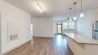 Located at 701 Watkins Centre Parkway in Midlothian, Virginia, this well-appointed 3-bedroom, 2-bathroom residence offers a thoughtfully designed single-floor layout with contemporary finishes throughout. The open-concept kitchen and living area serves as the heart of the home, featuring rich granite countertops, crisp white shaker cabinetry, a subway tile backsplash, stainless steel appliances, and pendant lighting over a generous kitchen island. Wood-look plank flooring flows seamlessly through the main living areas, complementing the bright, neutral palette. The living room is bathed in natural light from large windows and a glass-panel door, with a ceiling fan adding comfort overhead. The spacious primary bedroom features plush carpeting, a ceiling fan, and windows overlooking the exterior. Its en-suite bathroom is well-equipped with granite vanity counters, white cabinetry, a walk-in glass shower, and built-in shelving. The two additional bedrooms are similarly finished with soft carpeting, ceiling fans, and ample natural light. The second bathroom includes accessibility-friendly grab bars and wood-look flooring. Three closets provide generous storage throughout. A connecting hallway ties the layout together, creating a cohesive and functional living environment.