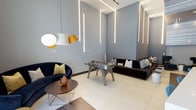 This contemporary single-floor space showcases a refined blend of modern design and recreational functionality. The room immediately draws attention with its soaring ceilings adorned with striking geometric LED light strips that run diagonally across the walls, creating a dramatic and visually dynamic atmosphere. The cool grey walls complement the clean, large-format porcelain tile flooring, contributing to a sleek, minimalist aesthetic throughout.

At the center of the space stands a full-size foosball table, serving as the focal point for entertainment and social interaction. Surrounding it is a thoughtfully curated seating arrangement, including a deep navy blue curved sofa accented with chartreuse throw pillows, and a plush dark sectional sofa dressed with an assortment of patterned cushions — both offering comfortable vantage points for guests and spectators alike.

A distinctive pendant light with a white exterior and warm gold interior adds an artistic touch, balancing the room's cool tones with a hint of warmth. A round wooden coffee table on a geometric metal base anchors the lounge area, completing the contemporary furnishing palette.

The overall ambiance is sophisticated yet inviting — a space designed to encourage both lively activity and relaxed social gatherings in equal measure.