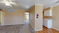 This single-story unit is laid out with a practical, functional design throughout. The entry area welcomes residents with parquet wood flooring that extends into the galley-style kitchen, which features white cabinetry with decorative raised paneling, light speckled countertops, a double-basin sink, a white electric range, and a full-size refrigerator — all set against warm golden-tan walls. Crown molding adds a subtle finishing detail throughout the unit.

The living areas transition from parquet flooring to plush carpet and are illuminated by natural light from multiple windows fitted with horizontal blinds. Ceiling fans are present throughout the main living and bedroom spaces, providing both lighting and air circulation. The textured popcorn ceilings are consistent across all rooms.

Multiple carpeted bedrooms offer comfortable proportions, each with neutral tan walls, white baseboards, and ceiling fans. The bedrooms connect via a carpeted hallway visible in the floor plan layout. Two bathrooms each include a full tub-and-shower combination with white surround panels and chrome fixtures. The overall ambiance is neutral and move-in ready, offering a clean, understated living environment.