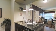 Located at 1 Parker Ave in Philadelphia's Manayunk neighborhood, this single-floor residence offers a thoughtfully designed open-concept layout that blends modern aesthetics with functional living. The kitchen serves as a central highlight, featuring dark cabinetry, striking granite countertops, and a peninsula with an undermount sink — ideal for both meal preparation and casual entertaining. Polished chrome pendant lights hang above the peninsula, adding an industrial-chic flair that complements the overall design. The kitchen flows seamlessly into the dining and living areas, creating a cohesive and spacious feel throughout the main living space. Neutral wall tones are accented by a bold dark feature wall, adding depth and visual contrast to the interior. The living area is warmly lit and comfortably appointed, with natural light filtering in through windows that brighten the space. The single-floor layout ensures easy accessibility and a natural sense of connectivity between all areas of the home. Overall, the space presents a polished, contemporary aesthetic that is well-suited for modern everyday living in the heart of Philadelphia.