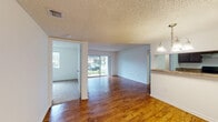 Located at 20879 NW Ninth Ct, Unit 108 in Miami Gardens, FL, this single-floor unit offers a practical and well-appointed layout. The open living and dining area is finished with warm hardwood-style flooring and features a textured ceiling, crisp white walls, and a sliding glass door that fills the space with natural light and provides direct outdoor access. A pass-through counter connects the living area to the kitchen, which is equipped with dark espresso cabinetry, granite-style countertops, stainless steel appliances including a range and refrigerator, and tile flooring. A dedicated laundry area with a full-size washer is conveniently accessible from the main living space, complemented by a chandelier light fixture overhead. The bedrooms are carpeted, offering a comfortable feel, with windows that bring in ample natural light. Two bathrooms serve the unit — one featuring a tiled walk-in shower with a dark vanity and granite countertop, and the other offering a full tub-shower combination with matching tile surround and similar vanity finishes. The thoughtful layout and mix of finishes throughout make this a functional and inviting single-story residence.