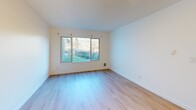 This one-bedroom, one-bathroom unit is located at 3630 Renton Ave S in Seattle's Rainier Valley neighborhood. The single-level layout makes efficient use of its intimate footprint, with light wood-tone flooring running throughout all rooms, creating a cohesive and clean aesthetic.

The entrance hall features a textured ceiling and a built-in closet, leading into the open kitchen and living area. The kitchen includes white cabinetry and a functional countertop layout that flows naturally into the living space, which is bathed in natural light from a large picture window overlooking lush greenery.

The bedroom is a comfortable, well-proportioned room featuring a sliding-door closet, a textured ceiling, and a window framing views of surrounding trees and landscaping — bringing a sense of calm and nature into the private retreat. A second closet provides additional storage in the hallway.

The bathroom is clean and straightforward, appointed with a full-size soaking tub and shower combination, a single vanity with white cabinetry, and a gold-framed mirror that adds a subtle accent. The overall palette throughout the unit is crisp white with warm wood tones, giving the space a bright, move-in-ready feel well-suited to efficient, comfortable urban living.
