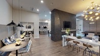 This sophisticated single-floor amenity space blends modern design with functional versatility across several distinct yet open-connected zones. The main lounge anchors the space with a dramatic floor-to-ceiling dark stacked-stone accent wall housing a linear fireplace and mounted flat-screen TV, complemented by a striking sputnik chandelier and plush navy seating arranged over an abstract area rug.

Adjacent to the lounge, a sleek bar and kitchen area features a curved white quartz island with gold wire barstools, pendant globe lighting, and a bold chevron-patterned tile feature wall with dual mounted screens — ideal for entertaining or casual gatherings. Full-height glass doors open directly to an outdoor patio, flooding the area with natural light.

A game room with geometric-patterned tile flooring, a pool table, and slatted wood ceiling detailing adds a relaxed recreational element to the space. Private conference and co-working rooms enclosed by sliding glass-panel doors offer a quiet retreat, equipped with wall-mounted displays and built-in cabinetry with white quartz countertops.

Throughout, wide-plank wood-look flooring, recessed lighting, curated artwork, and a cohesive gray and navy color palette unify the space, creating an upscale, community-centered environment designed for both productivity and leisure.