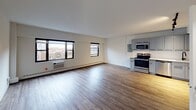 Located at 5815 N Sheridan Road in Chicago's vibrant Edgewater neighborhood, this single-floor unit offers a clean, modern aesthetic throughout its thoughtfully designed layout. The open-concept living and kitchen area is anchored by warm wood-look flooring and lined with large black-framed windows that allow natural light to fill the space while offering views of the surrounding neighborhood. A baseboard heating system and wall-mounted AC unit provide year-round climate control. The kitchen is a standout feature, showcasing gray shaker-style cabinetry with matte black hardware, white quartz countertops, a white subway tile backsplash, and a full suite of stainless steel appliances including an electric range, built-in microwave, dishwasher, and refrigerator. Track lighting overhead adds a contemporary touch. The bedroom features plush wall-to-wall carpeting, a window with outdoor views, and a calm, neutral palette. The bathroom is finished with floor-to-ceiling white tile, a soaking tub with a rainfall showerhead, a modern floating vanity with wood-toned cabinetry, and a mirrored medicine cabinet. Clean white walls and consistent finishes throughout give the space a cohesive, move-in-ready feel.