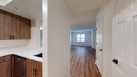 This Andover House one-bedroom apartment (A1E 0212) offers 640 square feet of efficiently designed living space. The layout includes a spacious 160 square foot bedroom, a full bathroom, a well-appointed kitchen, and an open-concept living area. The apartment features contemporary finishes throughout, with warm wood-toned flooring creating a cohesive look across all rooms. The kitchen boasts sleek wood cabinetry, white countertops, and stainless steel appliances, including a built-in microwave and electric range. The bathroom is equipped with a tub-shower combination, modern fixtures, and a wooden vanity. Large windows in the bedroom and living area provide ample natural light, while the neutral wall color enhances the sense of space. The apartment also includes convenient features such as a closet for storage and central air conditioning, as evidenced by the visible vent. This thoughtfully designed space offers a comfortable and stylish urban living experience.
