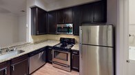 Located at Colony Oaks Drive in Charlotte, NC, this single-floor residence offers a well-designed layout that balances comfort and functionality. The kitchen is a standout feature, showcasing dark espresso cabinetry, granite countertops, a tile backsplash, and a full suite of stainless steel appliances, including a range, microwave, dishwasher, and refrigerator. Light hardwood-style flooring anchors the kitchen's refined aesthetic. A breakfast bar with elegant pendant lighting connects the kitchen to the open living and dining area, which is finished with crown molding, neutral walls, and plush carpeting that extends throughout the main living spaces. Natural light filters through windows fitted with blinds, enhancing the bright and airy ambiance. The bedrooms are generously sized, each featuring ceiling fans, soft carpeting, and windows that bring in views of the surrounding greenery. The bathrooms are clean and functional, with tiled tub-shower combinations, chrome fixtures, and wood-style flooring. The entry foyer provides a welcoming transition into the main living space. Overall, the residence presents a cohesive, neutral palette throughout, offering a move-in-ready environment suited for comfortable everyday living in the Charlotte area.