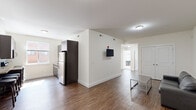 This well-designed 3-bedroom, 3-bathroom unit offers a clean, modern aesthetic across a single floor. The open-concept living and kitchen area serves as the heart of the space, featuring warm hardwood-style flooring and crisp white walls that create a bright, welcoming atmosphere. The kitchen is outfitted with dark cabinetry, stainless steel appliances including a full-size refrigerator and electric range, a mosaic tile backsplash, granite-style countertops, and a breakfast bar with seating — ideal for casual dining. A wall-mounted TV in the adjoining living area adds a practical touch to the shared space.

The three bedrooms are carpeted for comfort and are filled with natural light from exterior-facing windows. The primary bedroom is a well-proportioned private retreat, while the additional bedrooms offer ample space for furnishings and personal use.

Each of the three bathrooms is thoughtfully finished. One features a glass-enclosed walk-in shower with floor-to-ceiling tile, a floating vanity, and modern fixtures, while another offers a sliding glass shower enclosure with built-in shelving and white subway tile surround. Both reflect a consistent contemporary design language. The unit's efficient layout, modern finishes, and functional design make it a practical and comfortable living option.