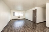 This single-floor unit offers a practical and functional layout across several well-defined rooms. The open living area is finished with durable wood-style plank flooring and features a ceiling fan overhead, along with dark baseboards that provide a clean contrast to the neutral white walls. A textured ceiling adds depth throughout. Natural light enters through a front-facing window, which also houses a wall-mounted air conditioning unit, complemented by baseboard heating along the perimeter walls.

The kitchen is a notable feature, outfitted with dark espresso-toned cabinetry, granite-style countertops, and a mosaic tile backsplash. A stainless steel sink, electric range, and refrigerator complete the functional cooking space, while a pendant light adds a finishing touch.

The bedrooms are carpeted for comfort, each with windows that bring in natural light and views of the surrounding neighborhood. One bedroom includes a built-in shelved closet, offering practical storage. The bathroom is clean and updated, featuring a gray vanity with a white countertop sink, tile flooring, and a wood-framed mirror above. Overall, the unit presents a straightforward, well-maintained living environment with a mix of updated finishes throughout.