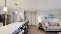 This single-floor residence offers a thoughtfully designed open-concept layout that seamlessly connects the kitchen, dining, and living areas. The kitchen is a standout feature, equipped with stainless steel appliances including a gas range, built-in microwave, refrigerator, and dishwasher. Crisp white cabinetry with modern hardware pairs elegantly with a classic subway tile backsplash and bright white countertops. A generous breakfast bar with seating for multiple occupants doubles as a dining area, illuminated by stylish pendant lighting that adds a contemporary touch. The living area is bright and welcoming, with wood-look flooring, crown molding, and a sliding glass door that allows natural light to pour in while providing access to an outdoor space. The bedroom is generously sized, featuring plush carpeting, dual sets of bifold closet doors for ample storage, and a large window that fills the room with natural light. The bathroom is finished with floor-to-ceiling marble-look tile, a combined tub and shower, and a sleek vanity with modern fixtures. Throughout the space, a neutral color palette and clean architectural lines create a cohesive, modern aesthetic.