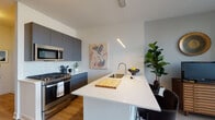 Located at 723 N Ogden Ave in Chicago's vibrant West Town neighborhood, this contemporary single-floor residence combines modern design with functional living. The open-concept kitchen is a standout feature, showcasing matte charcoal cabinetry, stainless steel appliances including a gas range, a marble-style backsplash, and a generous white quartz waterfall island with an undermount sink — ideal for both cooking and casual dining. Warm hardwood flooring flows throughout, tying the spaces together seamlessly. The living area is anchored by expansive floor-to-ceiling windows with sleek black frames, flooding the room with natural light and offering treetop views of the surrounding Chicago streetscape. Track lighting adds a modern, gallery-like touch overhead. The bedroom is a calm retreat, featuring large windows that bring in natural light and neighborhood views, with wood-tone flooring and thoughtful wall sconce lighting. The bathroom is finished with large-format marble-look tile in the glass-enclosed shower, a floating wood-grain vanity with a white countertop, and clean contemporary fixtures, creating a polished, spa-like atmosphere. This well-appointed space delivers refined urban living with stylish, high-quality finishes throughout.