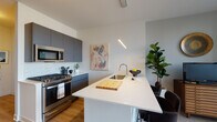 Located at 723 N Ogden Ave in Chicago's vibrant West Town neighborhood, this contemporary single-floor residence combines modern design with functional living. The open-concept kitchen is a standout feature, showcasing matte charcoal cabinetry, stainless steel appliances including a gas range, a marble-style backsplash, and a generous white quartz waterfall island with an undermount sink — ideal for both cooking and casual dining. Warm hardwood flooring flows throughout, tying the spaces together seamlessly. The living area is anchored by expansive floor-to-ceiling windows with sleek black frames, flooding the room with natural light and offering treetop views of the surrounding Chicago streetscape. Track lighting adds a modern, gallery-like touch overhead. The bedroom is a calm retreat, featuring large windows that bring in natural light and neighborhood views, with wood-tone flooring and thoughtful wall sconce lighting. The bathroom is finished with large-format marble-look tile in the glass-enclosed shower, a floating wood-grain vanity with a white countertop, and clean contemporary fixtures, creating a polished, spa-like atmosphere. This well-appointed space delivers refined urban living with stylish, high-quality finishes throughout.