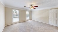 Located at 6300 Moseley Dixon Rd in Macon, GA, this single-floor, three-bedroom, two-bathroom home offers a practical and comfortable layout. The living room is generously sized, featuring plush carpeting, a ceiling fan with light fixture, and multiple windows that fill the space with natural light and offer outdoor views. Each of the three bedrooms continues the warm, neutral color palette with soft carpet flooring and ceiling fans for year-round comfort. The spacious primary bedroom includes a large closet with built-in wire shelving, providing excellent storage capacity, as well as an additional walk-in closet outfitted with multiple shelving tiers. The secondary bedrooms are well-proportioned, with one featuring floor-to-ceiling vertical blinds over a large window. Both bathrooms are equipped with a tub-shower combination and feature wood-look flooring. The full bathroom includes a vanity with a stone-topped countertop, white cabinetry, and a framed mirror. A hallway connects the rooms, creating an efficient and functional flow throughout the home. Clean white trim and neutral walls throughout contribute to a bright, cohesive aesthetic.