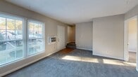 Located at 322 Clarence St in Charlotte, NC, this two-story home offers a functional and straightforward layout across two levels connected by a staircase. The main level features a spacious carpeted living area filled with natural light from large windows fitted with blinds, alongside a front entry door and easy access to the stairway leading to the upper floor. Wall-unit air conditioners and baseboard heating are present throughout, providing year-round climate control. The upper level hosts multiple carpeted bedrooms, each benefiting from individual windows that allow natural light to filter in. The rooms are finished with neutral-toned walls and clean white baseboards, creating a bright and versatile atmosphere. Two bathrooms serve the home: one features a full tub-shower combination with white tile surround and a frosted window, while the second bathroom, located on the upper floor, includes a tiled shower, hardwood flooring, a toilet, and a vanity beneath a textured ceiling. The overall aesthetic of the home is clean and functional, with consistent neutral tones, carpeted bedrooms, and ample natural light throughout both floors, making it a practical and comfortable residence in the Charlotte area.