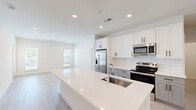 Located at 1801 Riverside Parkway in Douglasville, GA, this well-appointed 2-bedroom, 2-bathroom unit offers a thoughtfully designed single-level layout. The open-concept kitchen and living area serves as the heart of the home, anchored by a generous quartz waterfall island with an undermount stainless steel sink. The kitchen features crisp white upper cabinetry, gray lower cabinets, a white subway tile backsplash, and a full suite of stainless steel appliances including a French door refrigerator, electric range, and built-in microwave. Light wood-style flooring runs throughout the main living area, which is brightened by multiple windows and a glass-panel exterior door. Both bedrooms are carpeted and equipped with ceiling fans, offering a comfortable retreat. The primary bedroom includes an en-suite bathroom and a walk-in closet with multi-tier wire shelving for organized storage. The secondary bathroom features tile flooring and a tub-shower combination with white tile surround and a curved curtain rod. A dedicated laundry room with full washer and dryer hookups and wire shelving adds everyday convenience. Recessed lighting throughout contributes to the clean, modern aesthetic of this move-in-ready home.