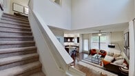 This two-story residence makes a striking first impression with its dramatic double-height ceilings in the main living area, where a carpeted staircase with a clean white balustrade draws the eye upward. The open-concept layout seamlessly connects the living room, dining space, and kitchen, all finished with rich hardwood-style flooring. Large windows flood the interior with natural light, while a ceiling fan adds a practical touch to the living room.

The kitchen is a standout feature, outfitted with dark espresso cabinetry, granite countertops, stainless steel appliances, and a central island with bar seating — ideal for casual dining or entertaining. Track lighting and pendant fixtures provide layered illumination throughout.

Two well-appointed bedrooms offer comfortable retreats, each with plush carpet, ceiling fans, and ample natural light from generously sized windows. The bathrooms are thoughtfully designed, featuring a tub-shower combination, granite vanity surfaces, hardwood-style flooring, and built-in shelving for added storage.

A convenient half bath is tucked beneath the staircase on the main level. Throughout the space, neutral wall tones and clean architectural lines create a versatile backdrop adaptable to a variety of interior styles.