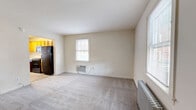Located at 303 Holly Dr in Middle River, MD, this three-floor home offers a functional and well-organized layout spread across three distinct levels. The main level welcomes you through a dedicated entrance that opens into a carpeted living room bathed in natural light from multiple windows. A wall-mounted A/C unit and a classic cast-iron radiator provide year-round comfort. Adjacent to the living room is the kitchen, which features warm honey-toned wood cabinetry, light granite-style countertops, wood-look vinyl flooring, and a full suite of black appliances including a refrigerator, range, microwave, and dishwasher. A staircase with a dark wood newel post and white balusters connects all three floors. The upper level hosts the bedroom, complete with plush carpeting, a ceiling fan, a radiator, and a window that allows natural light to fill the room. A full bathroom with a soaking tub, shower, vanity, and wood-look flooring is also found on this level. Multiple closets throughout the home provide generous storage. The lower level includes a basement, adding additional utility space. The home's neutral color palette and classic architectural details create a clean, approachable atmosphere throughout.