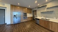 This well-appointed 940-square-foot, one-bedroom, one-bathroom apartment is thoughtfully designed with modern finishes throughout its single floor. The open-concept kitchen and living area serves as the heart of the unit, featuring dark hardwood-style flooring, high ceilings, and a sliding glass door that floods the space with natural light and provides access to an outdoor view. The kitchen is fully equipped with warm wood cabinetry extending to the ceiling, stainless steel appliances including a side-by-side refrigerator with ice maker, double wall ovens, a gas cooktop, and a dishwasher. Open metal shelving, a double undermount sink, and white quartz countertops complete the kitchen's contemporary aesthetic. The 240-square-foot primary bedroom features plush carpeting and a large floor-to-ceiling window wall offering expansive outdoor views and abundant natural light. The bathroom is spa-inspired, boasting a glass-enclosed walk-in shower with large-format dark tile, a soaking tub, dark wood vanity, and durable hardwood-style flooring. A dedicated in-unit laundry room includes a full-size washer and dryer. Dark baseboards and recessed lighting are consistent design elements found throughout the entire unit.
