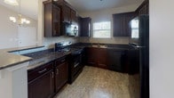 Located at 217 Carolina Forest Blvd in Jacksonville, NC, this single-floor home offers a thoughtfully designed layout with comfortable, functional living spaces throughout. The living room serves as a welcoming centerpiece, featuring vaulted ceilings, plush wall-to-wall carpeting, a ceiling fan, and elegant French doors that invite natural light and provide outdoor access. A chandelier adds a refined touch overhead, while a breakfast bar seamlessly connects the living area to the kitchen. The kitchen is outfitted with rich dark cabinetry, granite-style dark countertops, and a full suite of black appliances including a range, built-in microwave, and dishwasher. Stone-look vinyl flooring and a window above the sink complete this practical and stylish space. The bedrooms are generously sized, each featuring soft carpeting, ceiling fans, and windows that allow for natural light. The primary bedroom includes access to two separate rooms, providing closet and en-suite functionality. Both bathrooms feature stone-look vinyl flooring and tub-shower combinations, with the primary bathroom offering a granite-topped vanity and large mirror. A dedicated laundry area with cabinetry above the washer and dryer connections rounds out this well-equipped home.