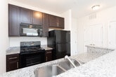 Located at 1065 Flats Ave in Mebane, North Carolina, this single-floor residence offers a clean, modern interior designed for comfortable everyday living. The open-concept layout is anchored by a well-appointed kitchen featuring dark espresso cabinetry, granite-style countertops, a breakfast bar peninsula, and black stainless appliances including a refrigerator, range, microwave, and dishwasher. Light wood-look flooring flows throughout the main living and kitchen areas, creating a cohesive and easy-to-maintain aesthetic. The living spaces are generously sized, with ceiling fans and windows fitted with blinds that allow abundant natural light to filter in throughout the day. Bedroom spaces are finished with plush carpet flooring, ceiling fans, and windows that invite warm, natural light. The bathroom is outfitted with a full soaking tub and shower combination set against clean white surrounds, complemented by wood-look flooring. Neutral wall tones throughout the home provide a versatile backdrop, while crisp white trim and millwork add a polished finishing touch. The overall ambiance is bright, clean, and move-in ready, offering a welcoming environment in a convenient Mebane location.