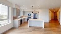 Located in Oxnard, CA, this well-appointed single-floor residence offers three bedrooms, two bathrooms, and a thoughtfully designed layout. The open-concept kitchen and living area serves as the heart of the home, featuring light wood-style flooring, recessed lighting, and large windows that invite natural light throughout. The kitchen is outfitted with gray shaker-style cabinetry, a subway tile backsplash, stainless steel appliances including a gas range and French door refrigerator, and a striking marble-look waterfall island illuminated by sleek pendant lights. Each bedroom is carpeted for comfort and equipped with a ceiling fan. The bedrooms offer generous proportions, with the primary bedroom providing a notably spacious retreat. Multiple windows frame outdoor views of the surrounding Oxnard landscape, including palm trees and open sky. Three closets, including well-built walk-in storage spaces, provide ample organization throughout. The two bathrooms feature clean, modern vanities with white countertops, light wood-tone flooring, and crisp white finishes. A dedicated laundry area and a balcony round out the functional amenities. The overall aesthetic is clean and contemporary, with a neutral palette of whites and soft grays creating a bright, move-in-ready atmosphere.