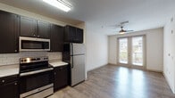 This single-floor unit offers a thoughtfully designed layout that seamlessly connects the kitchen and living areas. The kitchen is a standout feature, equipped with dark espresso cabinetry, a white subway tile backsplash, light quartz countertops, and a full suite of stainless steel appliances including a refrigerator, electric range, built-in microwave, and dishwasher. Wood-look flooring runs throughout, providing a warm and cohesive aesthetic across all rooms. The open living area is bright and airy, anchored by a ceiling fan and double French doors that lead to a private balcony, filling the space with natural light and offering views of the surrounding area. The bedroom is generously sized, featuring a ceiling fan, rich hardwood-style flooring, and two windows with blinds that allow ample natural light. The full bathroom includes a combination tub and shower, a single vanity with dark cabinetry, and consistent wood-look flooring that ties the space together. The overall ambiance is clean and modern, with a neutral color palette and practical finishes that make this a comfortable and functional living space.