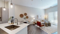 This thoughtfully designed 1-bedroom, 1-bathroom residence offers a modern open-concept layout that maximizes every inch of its footprint. The combined kitchen and living area serves as the heart of the home, anchored by a sleek kitchen island with quartz countertops and bar seating. The kitchen is outfitted with stainless steel appliances, flat-panel light wood cabinetry extending to the ceiling, and recessed pendant lighting that adds a contemporary touch. Wide-plank wood-style flooring flows throughout the main living area, complementing the neutral, warm-toned walls and soaring ceiling heights that lend a sense of openness well beyond the unit's compact scale. The living room benefits from a large sliding window that fills the space with natural light and offers views of greenery outside. The bedroom continues the airy aesthetic with tall ceilings, plush carpet flooring, and generous windows. A dedicated closet provides practical storage. The bathroom features a wood-toned vanity with a white quartz countertop, an undermount sink, and a full tub-shower combination. Throughout the residence, the design maintains a cohesive, contemporary aesthetic with clean lines and a neutral palette.