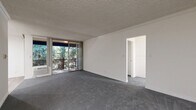 Located in the Northridge neighborhood of Los Angeles, this one-bedroom, one-bathroom unit offers a thoughtfully arranged layout across a single floor. The spacious living room features plush grey carpeting, crown molding, and a textured ceiling, with a sliding glass door that opens directly onto a private balcony overlooking lush greenery, filling the space with natural light. A separate dining room provides a dedicated area for meals, seamlessly connecting the living and kitchen areas. The galley-style kitchen is equipped with white cabinetry, a coil electric range, under-cabinet ventilation, a single-basin sink, and light wood-tone flooring that adds warmth to the space. The generously sized bedroom is carpeted and well-lit, offering ample room for furnishings, and includes its own sliding door access to the balcony. A dedicated closet provides convenient storage. The bathroom features light wood-tone flooring, a tiled vanity countertop with built-in drawers, a framed mirror, and a tub-shower combination with glass sliding doors. A built-in vanity nook adjacent to the bathroom adds a functional grooming area. Hallways connect each room efficiently, contributing to a practical and cohesive flow throughout the unit.