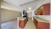This single-floor residence is thoughtfully laid out to maximize functionality and comfort throughout. The galley-style kitchen serves as a central highlight, featuring rich cherry wood cabinetry, light granite-style countertops, and stainless steel appliances including a refrigerator, electric range, and over-the-range microwave. A peninsula counter extends toward the living area, creating a natural transition between the kitchen and the open-plan living space. Light wood-style flooring runs through the kitchen, complemented by soft, neutral-toned carpet in the living areas and bedrooms, adding warmth underfoot.

The spacious living area offers generous room for furnishings and is bathed in a clean, neutral palette that lends itself to a variety of interior styles. A pendant light fixture provides a subtle decorative touch. The bedroom is well-proportioned and features two side-by-side closets with bifold doors and built-in rods, offering ample storage and organization.

Two bathrooms serve the unit, each finished with light beige ceramic tile flooring, white fixtures, and wall-mounted medicine cabinet mirrors. The bathrooms are clean and efficiently designed, with one featuring a vanity with cabinet storage. Overall, the unit presents a practical and well-maintained living environment with a cohesive, understated aesthetic throughout.
