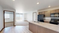 Located at 2109 E Anamosa St in Rapid City, South Dakota, this efficiently designed one-bedroom, one-bathroom unit offers a functional and comfortable single-floor layout. The open-concept kitchen is a central feature, equipped with a peninsula island that includes a double-basin sink, warm brown cabinetry, light countertops, and black appliances including a refrigerator, range, and over-the-range microwave. The kitchen flows seamlessly into the living area, which is finished with light wood-style flooring and receives generous natural light through a sliding glass door that opens to a private balcony with open views of the surrounding Rapid City landscape. The bedroom is carpeted for comfort and features a large window that brings in natural light and frames outdoor views. The full bathroom includes a combined tub and shower unit with tile flooring, providing clean and practical finishes throughout. A dedicated laundry room comes equipped with a full-size washer and dryer, as well as built-in wire shelving for additional storage. The unit's clean, neutral palette and practical layout make it a well-organized and functional living space.