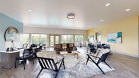 This thoughtfully designed single-floor community space offers a generous and versatile layout across two distinct areas. The entrance welcomes visitors into a bright, open lounge characterized by herringbone-patterned flooring, recessed lighting, and a striking teal accent wall adorned with large circular artwork. Expansive windows and glass doors flood the space with natural light while offering views of lush greenery and an adjacent outdoor balcony area. Comfortable seating arrangements anchor the lounge, complemented by a dedicated workstation area with warm yellow accent walls and contemporary artwork, creating an inviting yet functional reception environment.

The game room is a standout feature, combining leisure and social gathering in one dynamic space. A stacked stone fireplace with a mounted TV serves as a dramatic focal point, flanked by bold geometric wallpaper and pendant lighting above a sleek bar counter with bar seating. A large communal high-top table with copper-accented stools centers the room, while a shuffleboard table, foosball table, and additional seating provide ample entertainment options. The consistent herringbone flooring ties both areas together seamlessly, delivering a cohesive, modern aesthetic throughout the entire space.