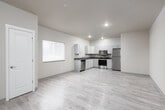 This well-appointed single-floor unit offers a clean, modern design throughout. The open-concept layout seamlessly connects the kitchen and living area, creating a bright and functional space. Light hardwood-style flooring extends across the main living areas, complementing the neutral warm-beige walls and white trim for a cohesive, contemporary aesthetic.

The kitchen is thoughtfully equipped with a full suite of stainless steel appliances, including a Whirlpool electric range, over-the-range microwave, full-size refrigerator, and a dishwasher. White shaker-style cabinetry provides ample storage, while gray countertops offer generous prep space. A stainless steel sink with a pull-down faucet completes the kitchen's practical design.

The living area is generously sized, offering flexible room for various furniture configurations. A sliding glass door leads directly to an outdoor patio, filling the space with natural light and providing convenient outdoor access.

The bathroom features full floor-to-ceiling tile surrounding a soaking tub and shower combination, paired with a vanity featuring a dark countertop and a large mirror. Recessed lighting throughout the unit ensures consistent, even illumination. The space also includes multiple interior doors leading to additional rooms, as well as a dedicated entry with a private exterior door.