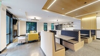 Located at 657 22nd Avenue Northeast in Minneapolis, MN, this thoughtfully designed single-floor space offers a generous, open-concept layout that seamlessly blends functional and social areas. The interior is finished with polished concrete floors that run throughout, contributing to the space's clean, modern aesthetic.

The kitchen is a standout feature, outfitted with sleek grey cabinetry, white quartz countertops, a large central island with bar seating, and a stainless steel French door refrigerator. A geometric white tile backsplash adds texture, while open wood-toned shelving displays curated décor. Pendant lighting above the island and abundant recessed lighting ensure the kitchen is both practical and visually striking.

Adjacent to the kitchen, a built-in banquette dining area with upholstered booth seating and wood accents provides a cozy gathering spot. The lounge area features bold yellow and grey upholstered furniture, a patterned area rug, a wall-mounted fireplace, and a large flat-screen TV. Large black-framed windows throughout the space invite ample natural light and offer views of surrounding greenery. A warm wood-paneled ceiling detail with integrated linear lighting adds architectural depth, and a circular chandelier anchors the lounge with a refined, contemporary touch.
