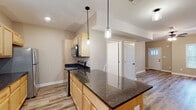 This two-story home offers a thoughtfully designed layout that balances functionality and comfort across both levels. The heart of the main floor is the galley-style kitchen, which features light maple cabinetry, dark granite countertops, stainless steel appliances, and a peninsula with pendant lighting overhead — ideal for both cooking and casual dining. Wood-look luxury vinyl plank flooring extends throughout the main level, lending a clean, cohesive feel. The open living area is generously proportioned, bathed in natural light, and anchored by a ceiling fan. A carpeted staircase leads to the upper level. A convenient half bathroom on the main floor includes a pedestal sink and wood-look flooring. Upstairs, the bedrooms are carpeted for added warmth and comfort, with each room featuring ceiling fans and ample natural light from well-placed windows with views to the outdoors. A full bathroom on the upper level includes a vanity with granite countertops, a tub-shower combination, and wood-look flooring. Neutral warm-toned walls throughout the home create a bright, welcoming ambiance that suits a wide range of interior styles.