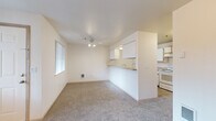 This single-floor, 2-bedroom, 2-bathroom residence offers a practical and comfortable layout with consistent neutral tones and carpet flooring throughout. The combined living room and kitchen area forms the heart of the home, where a peninsula-style pass-through kitchen features white cabinetry with wood-tone accents, a countertop range, refrigerator, and ample storage. A ceiling fan with light fixture illuminates the living area, which also benefits from a large window that draws in natural light. A separate living space showcases a tile-surround fireplace paired with track lighting and an additional window with outdoor views, providing a warm and inviting atmosphere. A hallway connects the main living areas to the two bedrooms, each carpeted and featuring large windows with vertical blinds that allow generous natural light and views of the surrounding greenery. The primary bedroom connects to a walk-in closet with built-in shelving on both sides and direct access to an en-suite bathroom featuring a shower stall, a vanity with under-sink storage, a large mirror, and tile flooring. The second bathroom includes a full bathtub and tiled flooring. A dedicated closet provides additional storage within the unit.