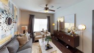 This thoughtfully designed single-floor residence combines contemporary style with functional living across a well-organized layout. The open-concept kitchen is outfitted with dark textured cabinetry, black appliances, a tile mosaic backsplash, granite countertops, and track lighting — creating a sleek, modern workspace. It flows seamlessly into the dining area, where rich hardwood-style flooring and direct sightlines to the living space make entertaining effortless.

The living room is a standout, featuring a ceiling fan, large windows dressed with floor-length draping curtains that invite natural light, and hardwood-style flooring. A substantial dark wood credenza anchors one wall, while the curated décor — including gold-toned artwork, sunburst mirrors, and layered soft furnishings — lends the space a refined, contemporary ambiance.

The bedrooms are carpeted and comfortably proportioned, each equipped with ceiling fans and natural light from well-positioned windows. The primary bedroom includes access to a spacious walk-in closet with built-in shelving and hanging storage. The bathroom features dark espresso cabinetry, granite countertops, a generous mirror, and a wall-mounted storage cabinet, all finished with clean, modern hardware throughout.