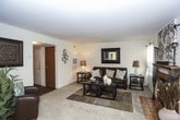 This single-floor residence offers a thoughtfully designed layout with a comfortable and cohesive aesthetic throughout. The spacious living room serves as the heart of the home, anchored by a tile-surround fireplace flanked by two windows that invite natural light and outdoor views. Neutral carpet, warm-toned walls, and classic furnishings contribute to an inviting ambiance.

Adjacent to the living room, a dedicated dining area accommodates a full-sized table and chairs beneath a ceiling fan, with large windows and access to an outdoor space, making it ideal for everyday dining or entertaining. The galley-style kitchen features warm wood cabinetry, white appliances, light countertops, and hardwood-style flooring, with a window above the sink providing additional natural light.

The primary bedroom is generously sized with plush carpet, a large window with drapery, and direct access to an en-suite bathroom. A second bedroom offers ample space, natural light, and a sliding-door closet with built-in storage. Both bedrooms feature neutral tones and soft carpet flooring.

The bathroom includes a tub-shower combination, a wood-toned vanity, and hardwood-style flooring, offering a clean and functional design. Overall, this residence provides a well-balanced blend of comfort, practicality, and classic style across every room.
