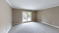 Located at 6530 Davidson St in Columbia, SC, this single-floor home offers three bedrooms and three bathrooms within a well-organized layout. The combined kitchen and living room serves as the heart of the home, with the kitchen featuring white shaker-style cabinetry, granite-look countertops, stainless steel appliances including a full-size refrigerator and dishwasher, and light tile flooring accented by crown molding. The living room is carpeted and finished with crown molding, and opens directly to an outdoor balcony through a sliding glass door, allowing for natural light and views of the surrounding greenery. The primary bedroom is generously sized, featuring dual windows, a ceiling fan, plush carpet, and ample natural light. A second bedroom offers a large double-door closet and direct hallway access. All bedrooms maintain a neutral taupe color palette with white trim throughout. The bathrooms are well-appointed, with one featuring warm hardwood flooring, a wide white vanity with a large mirror and brushed nickel lighting, and access to a tiled tub-shower combination. The layout is completed by a connecting hallway, providing functional flow between all rooms.