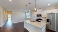 This single-story home presents a thoughtfully designed layout with a clean, modern aesthetic throughout. The heart of the home is an open-concept kitchen and living area, where rich dark hardwood flooring sets a warm foundation. The kitchen is outfitted with crisp white shaker cabinetry, light granite countertops, a central island with an undermount sink, and a full suite of stainless steel appliances including a side-by-side refrigerator, electric range, and built-in microwave. Three stylish pendant lights hang above the island, adding both function and character. Large windows flood the space with natural light and offer views of the surrounding greenery.

The bedrooms are carpeted for comfort and each include a ceiling fan with light fixture and windows with blinds that invite natural light. Several bedrooms feature access to closets or adjoining spaces, offering practical storage solutions. The bathrooms are finished with granite-topped white vanities and undermount sinks, while at least one bathroom includes a walk-in shower with tiled surround and brushed nickel hardware.

Completing the home is an attached garage with a polished concrete floor, housing the water heater and electrical panel, providing convenient utility access. The overall palette of neutral tones and consistent finishes creates a cohesive, move-in-ready environment.