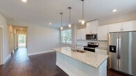 This single-story home presents a thoughtfully designed layout with a clean, modern aesthetic throughout. The heart of the home is an open-concept kitchen and living area, where rich dark hardwood flooring sets a warm foundation. The kitchen is outfitted with crisp white shaker cabinetry, light granite countertops, a central island with an undermount sink, and a full suite of stainless steel appliances including a side-by-side refrigerator, electric range, and built-in microwave. Three stylish pendant lights hang above the island, adding both function and character. Large windows flood the space with natural light and offer views of the surrounding greenery.

The bedrooms are carpeted for comfort and each include a ceiling fan with light fixture and windows with blinds that invite natural light. Several bedrooms feature access to closets or adjoining spaces, offering practical storage solutions. The bathrooms are finished with granite-topped white vanities and undermount sinks, while at least one bathroom includes a walk-in shower with tiled surround and brushed nickel hardware.

Completing the home is an attached garage with a polished concrete floor, housing the water heater and electrical panel, providing convenient utility access. The overall palette of neutral tones and consistent finishes creates a cohesive, move-in-ready environment.