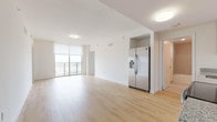 This single-floor unit showcases a clean, contemporary design defined by light hardwood flooring that runs seamlessly throughout the living spaces, creating a bright and cohesive aesthetic. The open-concept living and dining area is generously proportioned, benefiting from floor-to-ceiling sliding glass doors that lead to a private balcony, framing expansive outdoor views of the surrounding cityscape. Natural light floods the interior, enhancing the airy, neutral-toned palette of white walls and light wood finishes.

The kitchen is efficiently designed with flat-front cabinetry in a warm taupe wood finish, granite countertops, and a full suite of stainless steel appliances, including a French door refrigerator with an in-door ice and water dispenser, a dishwasher, electric range, and built-in microwave. A dedicated bedroom features its own access to a balcony area, adding an additional outdoor connection. The primary bedroom includes direct access to a well-appointed ensuite bathroom, along with a separate closet. The bathroom is finished with large-format tile flooring, a granite-topped vanity with warm wood cabinetry, and a tiled soaking tub and shower combination. The overall ambiance is modern, light-filled, and functional.
