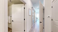 This single-floor residence combines modern design with functional living. The hallway serves as a central spine, finished in crisp white walls and light wood-look flooring, and features panel-style doors with matte black hardware alongside a striking sliding barn door with frosted glass panels that adds a contemporary touch while providing privacy to adjoining spaces.

The kitchen is well-appointed with a two-tone design pairing white upper cabinetry with warm wood-grain lower cabinets and a matching island. Stainless steel appliances, including a full-size refrigerator, range, microwave, and dishwasher, provide modern functionality, while subway tile backsplash and white quartz countertops complete the polished aesthetic. Pendant lighting adds warmth overhead.

The bedroom offers a calm retreat with vaulted ceiling detail, light wood flooring, a built-in closet with sliding panel doors, and neutral tones throughout. The bathroom features a wood-tone vanity with white countertop, large-format marble-effect tile in the tub surround, and matte black fixtures that tie cohesively to the rest of the unit's design language.

The living area rounds out the space with clean white walls and warm mid-century modern furnishings, creating an inviting and cohesive atmosphere throughout.